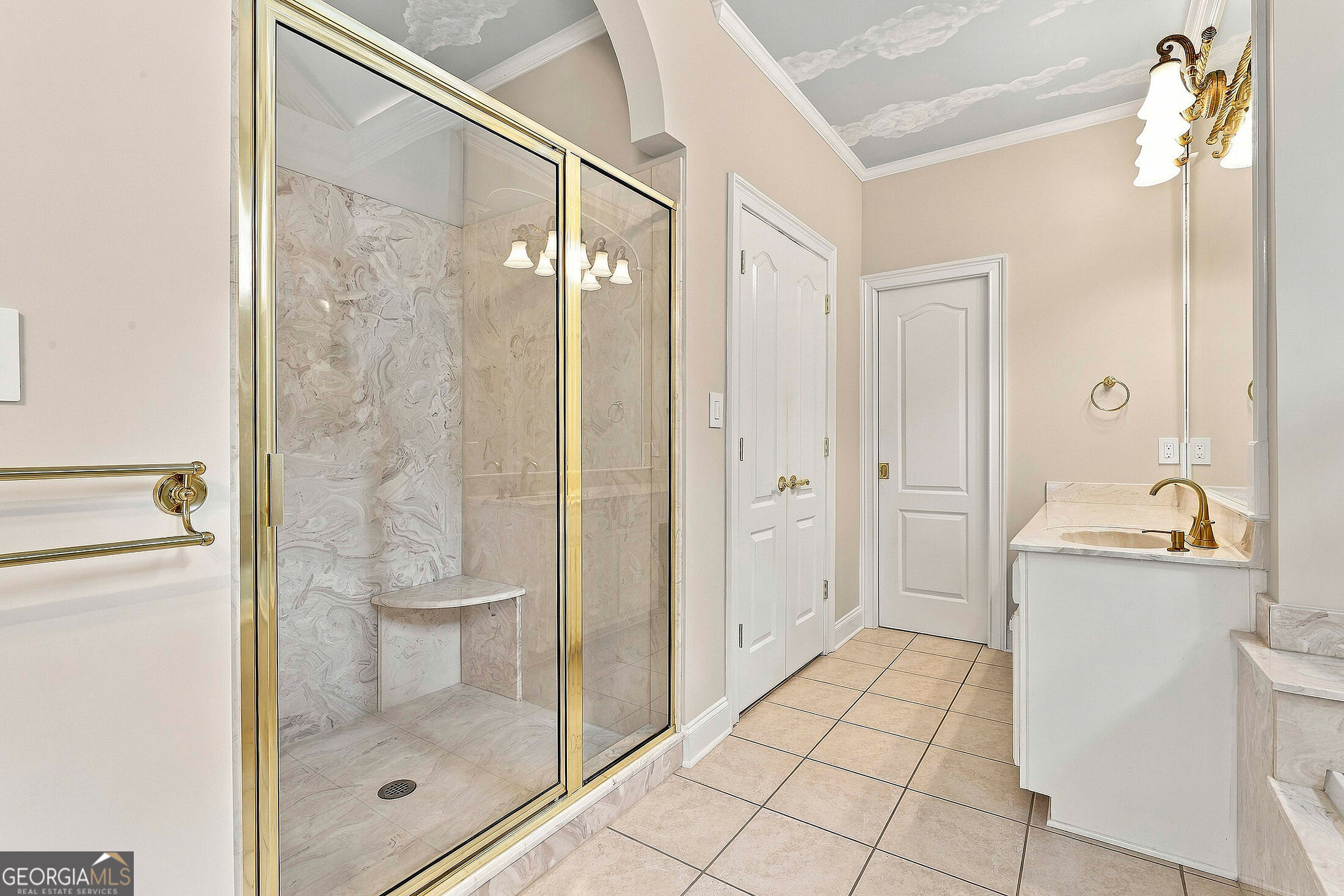 Bathroom with a gold-framed glass shower, marble-patterned tile, and white vanity with gold fixtures.