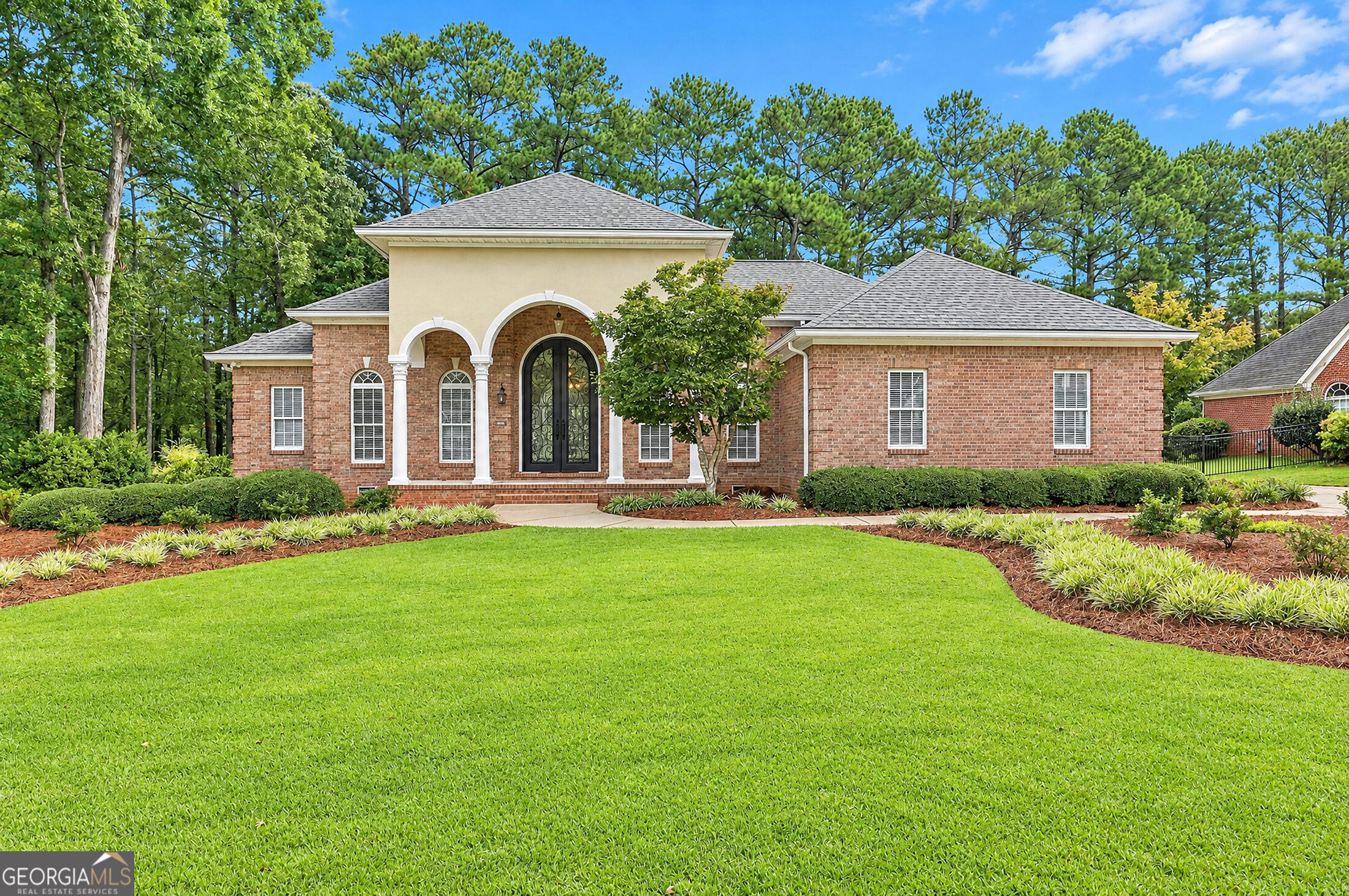 Brick house with an arched entry, broad green lawn, and mature trees.