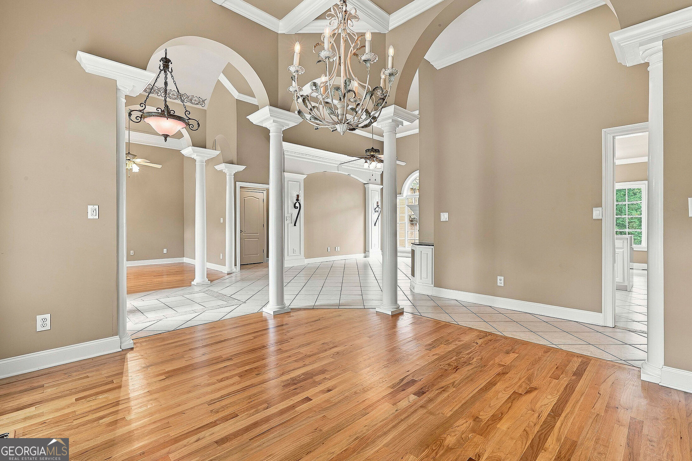 Vacant interior with hardwood floors, white columns, arched openings, and a chandelier.