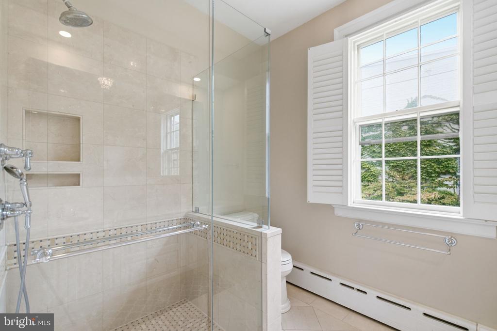 Bathroom with a glass-enclosed tiled shower and a large shuttered window overlooking trees.