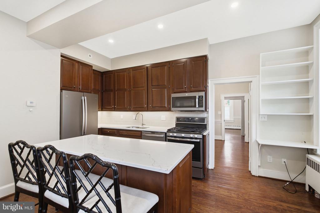 Kitchen with a white island and bar seating, dark wood cabinets, stainless appliances, and built-in shelving.