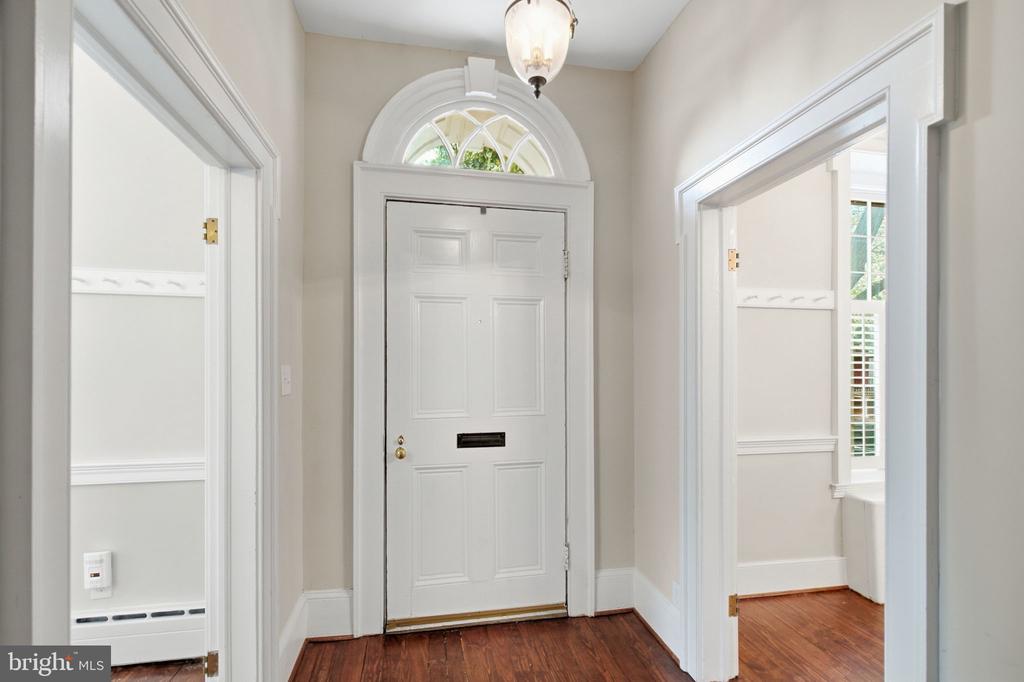 Entry foyer with a white paneled front door, arched transom, and dark hardwood floors.