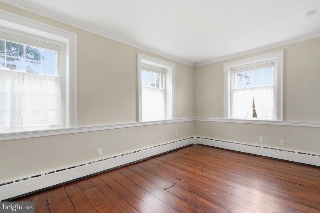 Empty room with three tall windows, white chair rail, and polished reddish-brown hardwood floors.