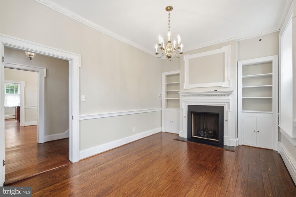 Vacant living room with a white fireplace, built-in shelves, chandelier, and hardwood floors.