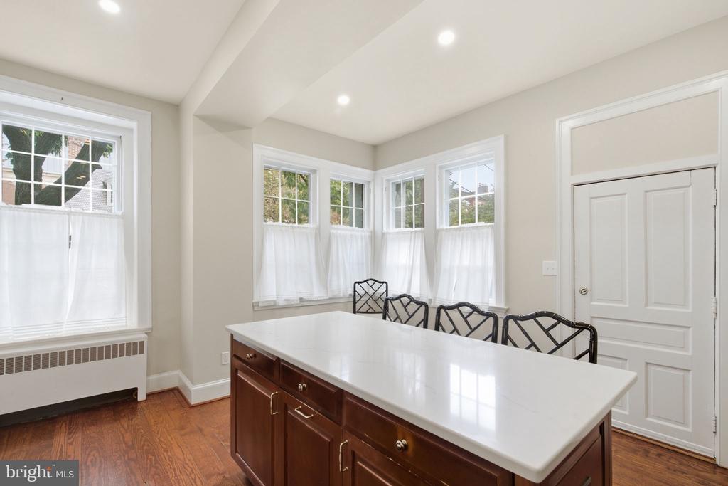 Kitchen with a long white-countered island, dark wood cabinetry, black chairs, and multiple windows.