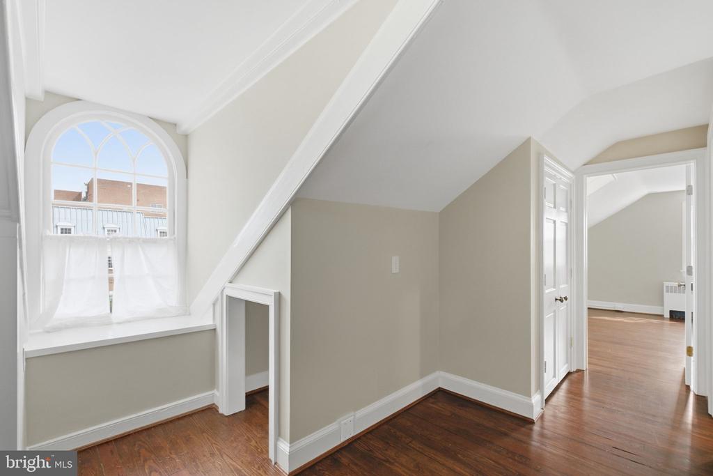 Empty room with a sloped ceiling, arched curtained window, and dark hardwood floors.