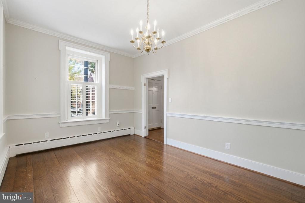 Empty room with hardwood floors, a tall shuttered window, and a brass chandelier.