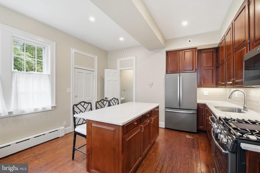 Kitchen with a white-topped island, dark wood cabinetry, stainless steel appliances, and hardwood floors.