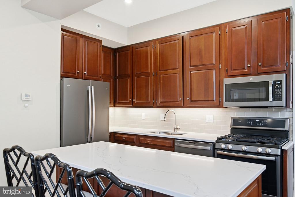 Kitchen with rich wood cabinets, stainless appliances, and a large white island with black stools.