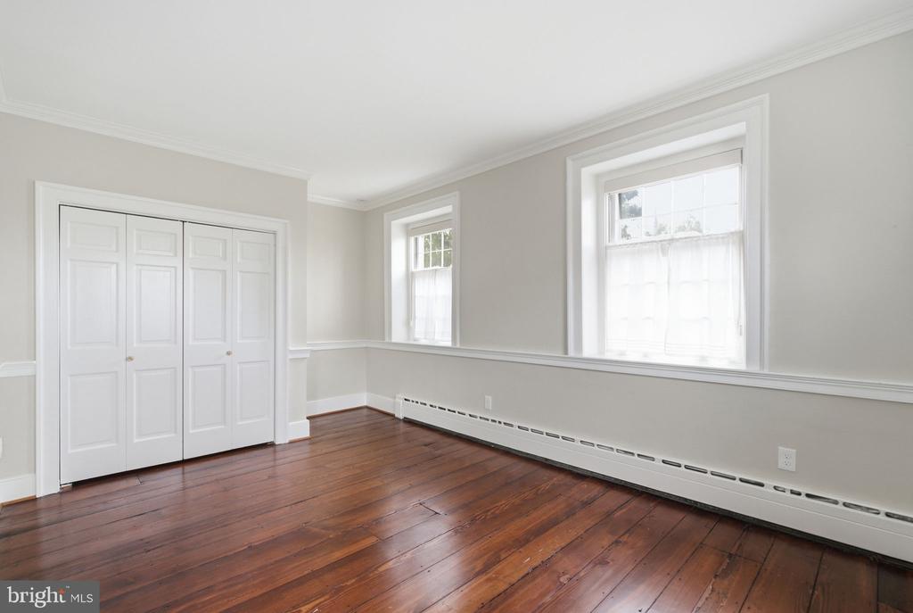 Empty room with polished hardwood floors, a paneled closet, and two tall windows.
