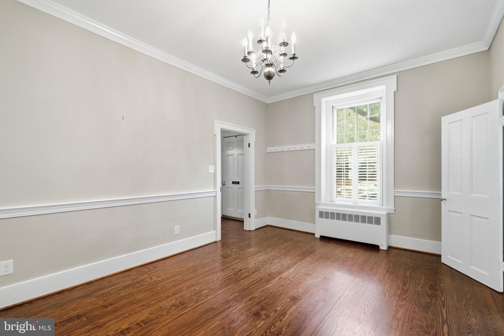 Empty room with hardwood floors, a chandelier, and a tall shuttered window.