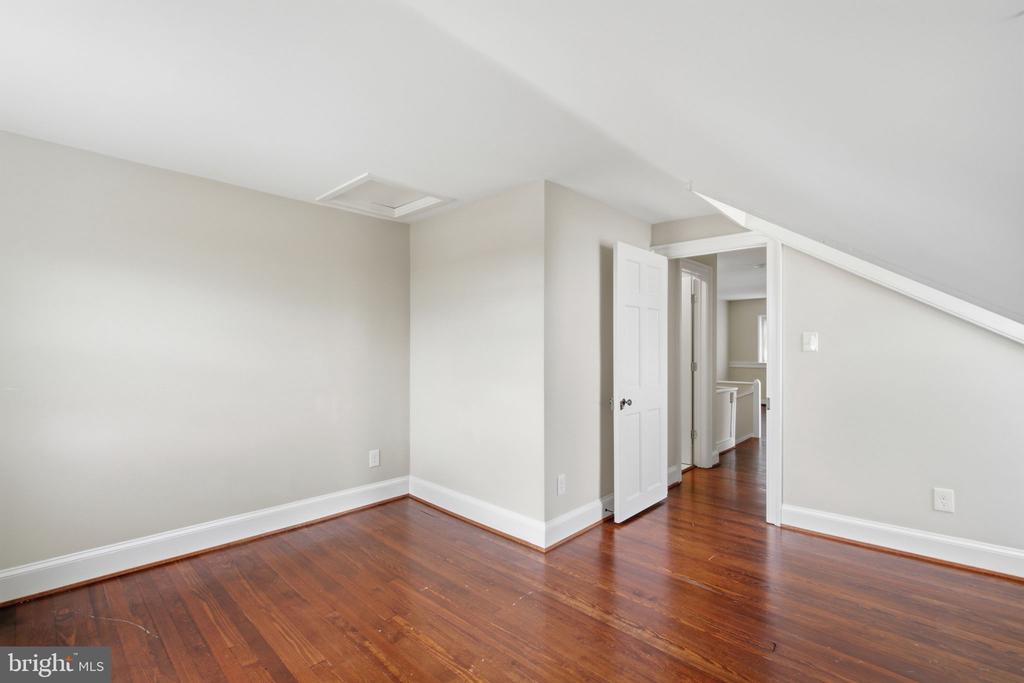 Empty upstairs room with hardwood floors, a sloped ceiling, and an open doorway.
