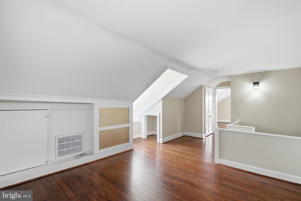 Finished attic room with a sloped ceiling, hardwood floors, and built-in storage.