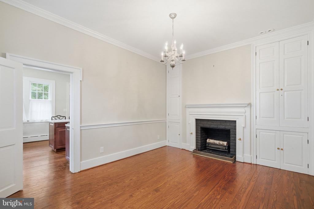 Empty room with hardwood floors, a fireplace, built-in cabinets, and a chandelier.
