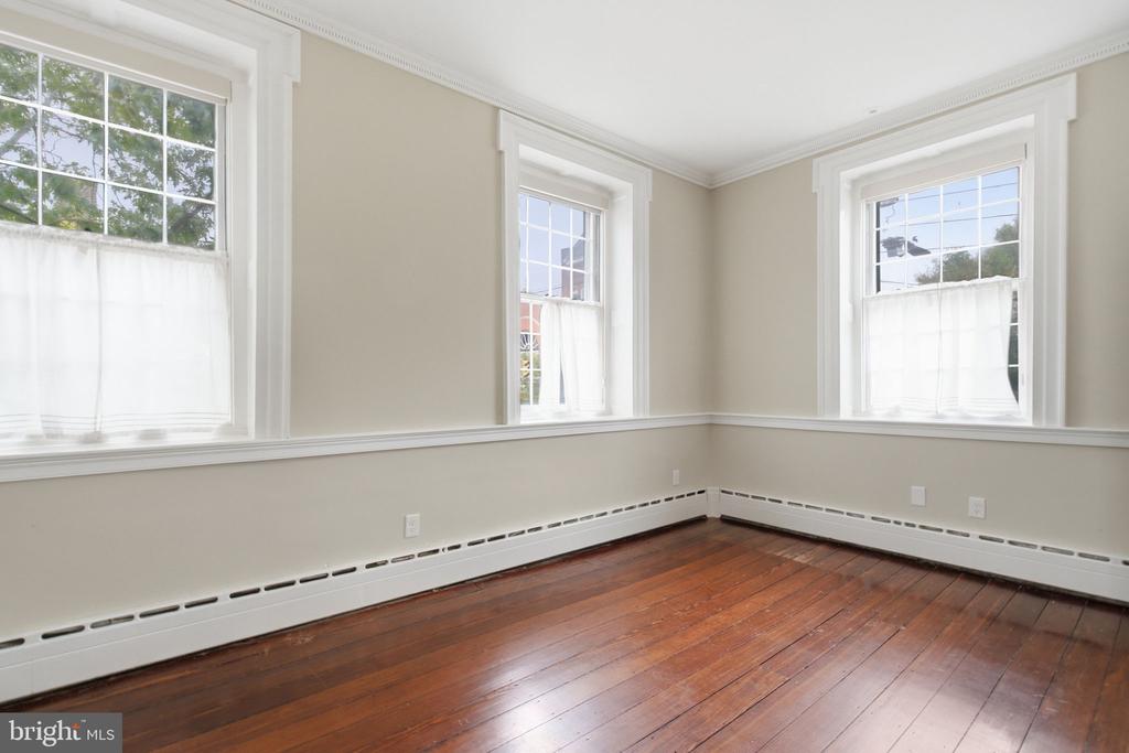 Empty room with hardwood floors, three tall sash windows, and ornate white trim.