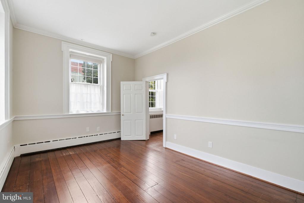 Vacant room with polished hardwood floors, beige walls, and tall windows.