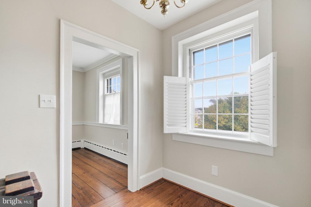 Empty room with hardwood floors and a large window with open white shutters.