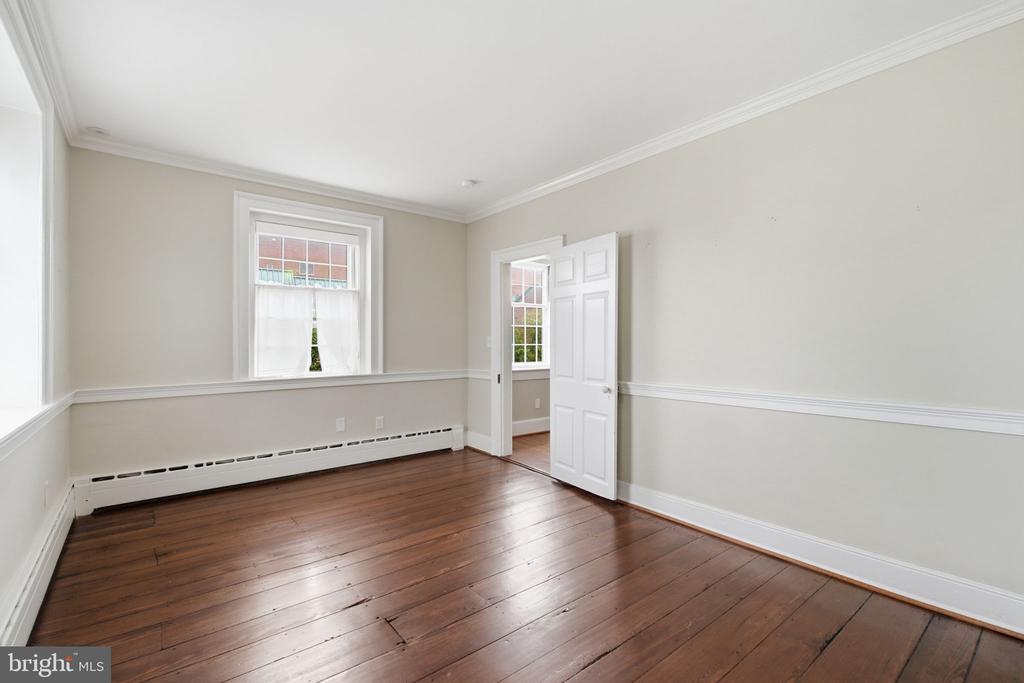 Empty room with dark wood floors, pale walls, and an open door to an adjoining room.