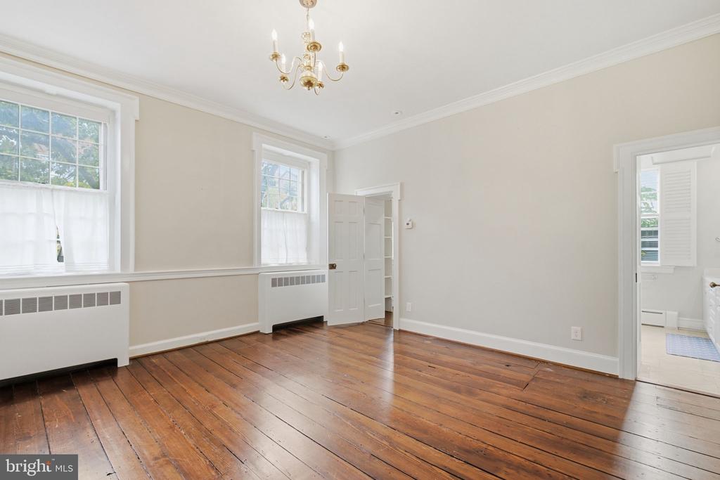 Empty room with wide-plank wood floors, tall windows, and a chandelier.