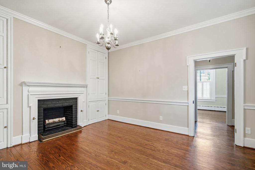 Unfurnished room with a white fireplace, built-in cabinets, hardwood floors, and a chandelier.