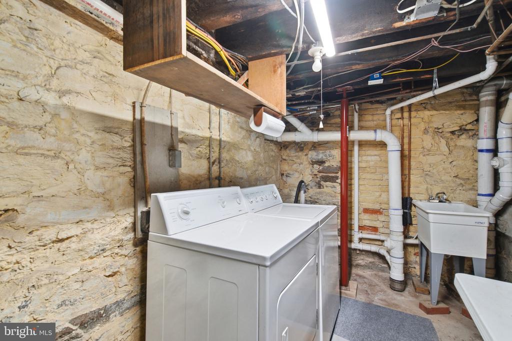 Basement laundry area with washer, dryer, utility sink, and exposed stone walls.