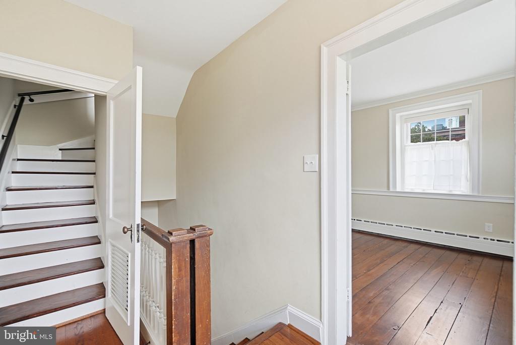 Upstairs hallway with a white staircase and an adjoining room with hardwood floors.