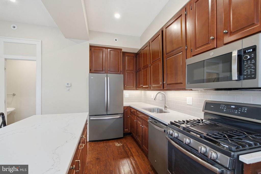 Kitchen with dark wood cabinets, white countertops, stainless steel appliances, and hardwood floors.