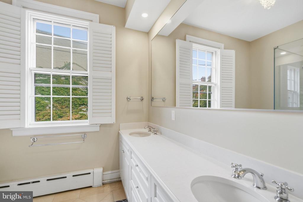 Bathroom with a long white double-sink vanity, large mirror, and shuttered windows.