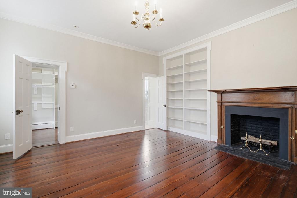Empty room with a wood fireplace, built-in bookshelves, and polished hardwood floors.