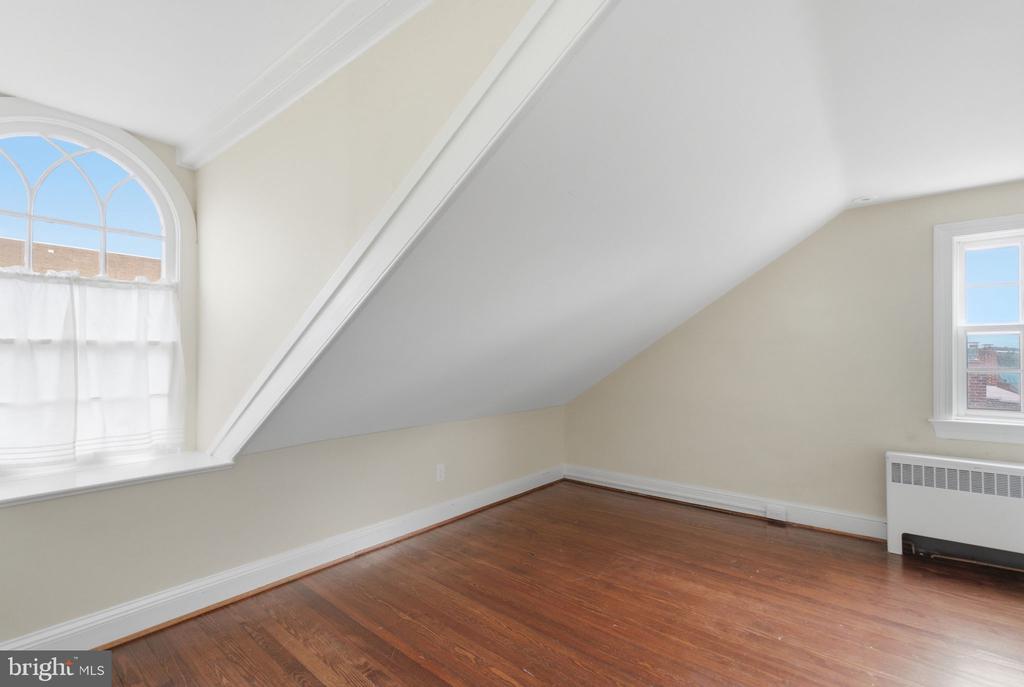 Empty upper-floor room with hardwood floors, a sloped ceiling, and an arched window.