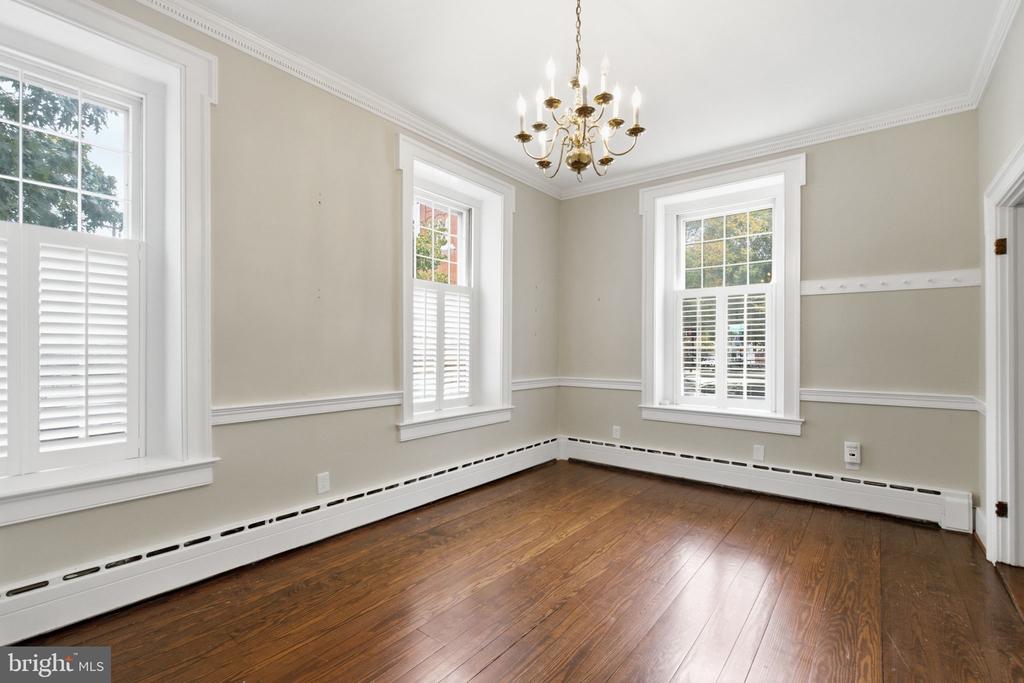 Empty room with polished hardwood floors, tall shuttered windows, and a brass chandelier.