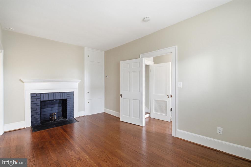 Vacant room with hardwood floors, a black brick fireplace, and open white paneled doors.