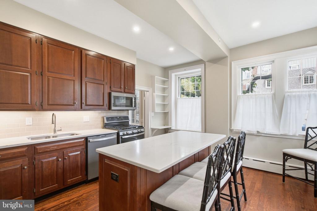 Kitchen with cherry cabinets, stainless steel appliances, a large island, and tall curtained windows.