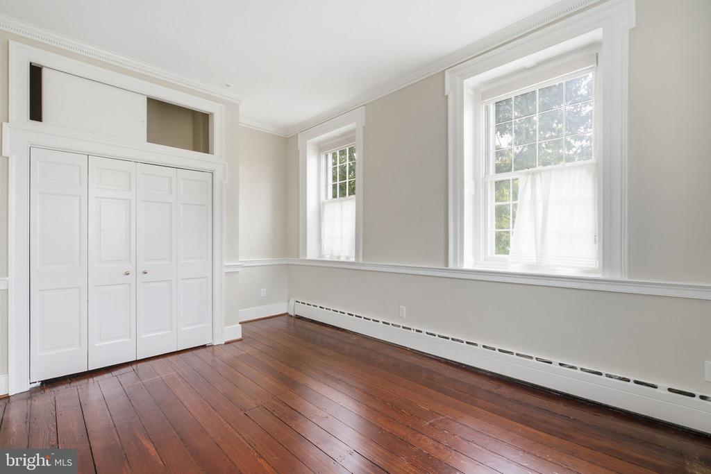 Empty room with white built-in closets, tall windows, and polished hardwood floors.