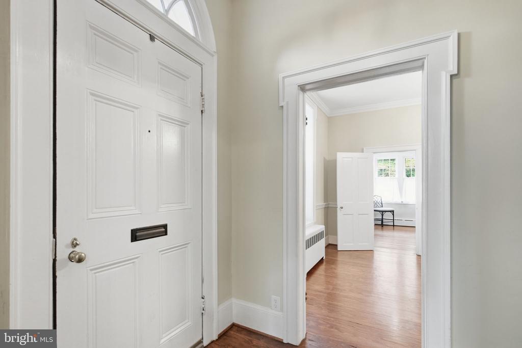 Entry foyer with a white paneled front door and hardwood floors leading into a bright adjoining room.