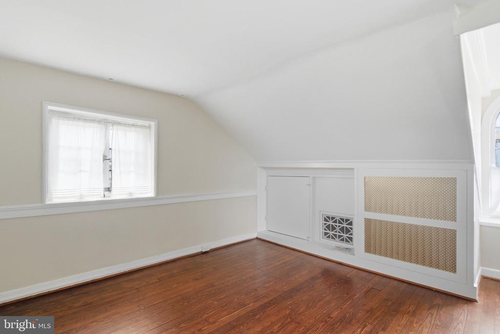 Vacant attic room with polished hardwood floors, a sloped ceiling, and built-in knee-wall cabinets.