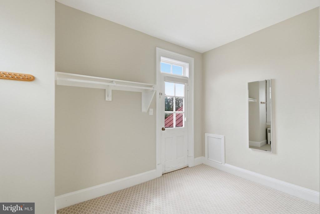 Empty carpeted closet with a long white shelf, wall mirror, and glazed door.