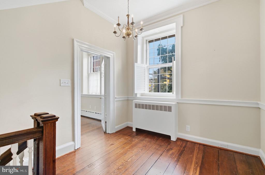 Empty room with polished hardwood floors, a tall shuttered window, and a chandelier.