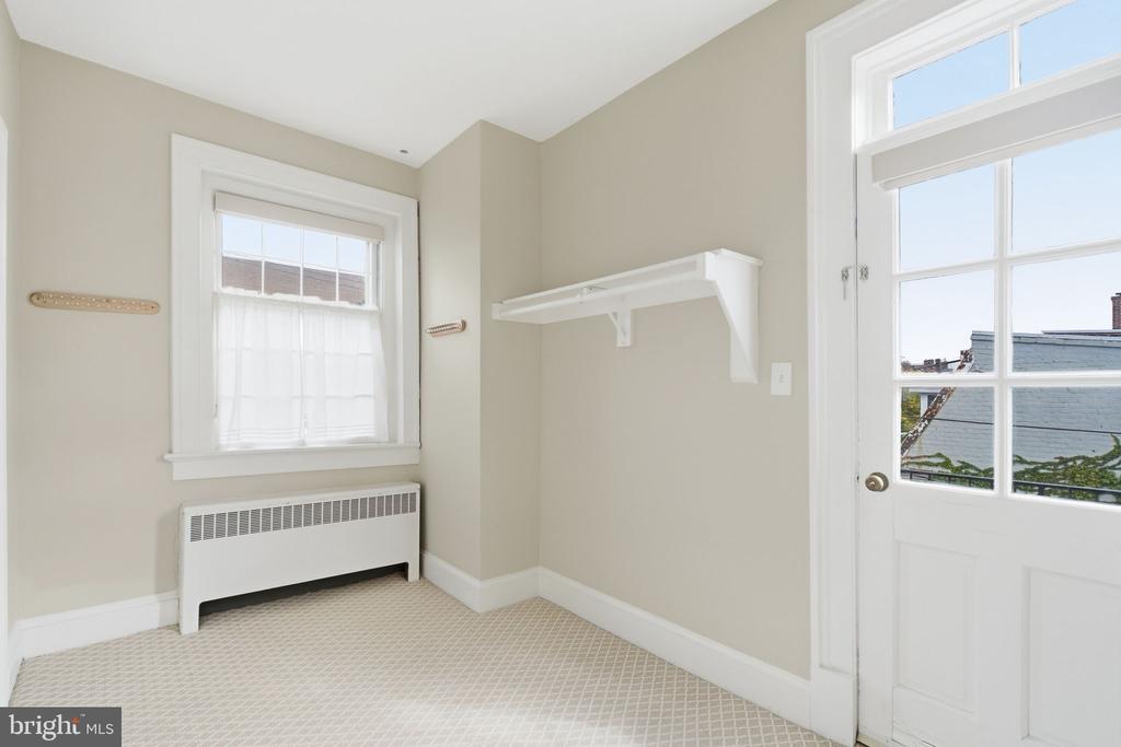 Vacant room with a wall shelf, radiator beneath the window, and a glazed exterior door.