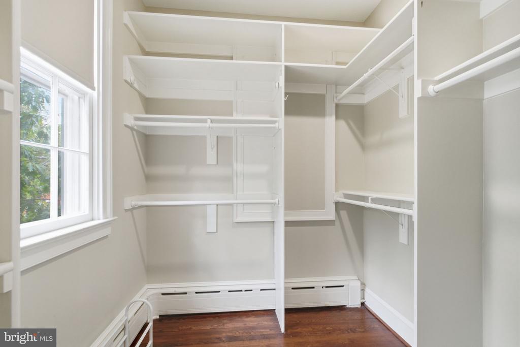 Walk-in closet with built-in shelving, hanging rods, a window, and dark hardwood floors.