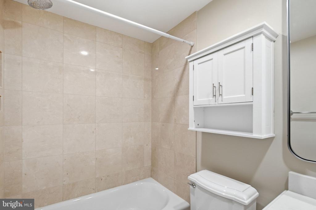 Bathroom with beige tiled walls, a white bathtub, toilet, and wall-mounted cabinet.