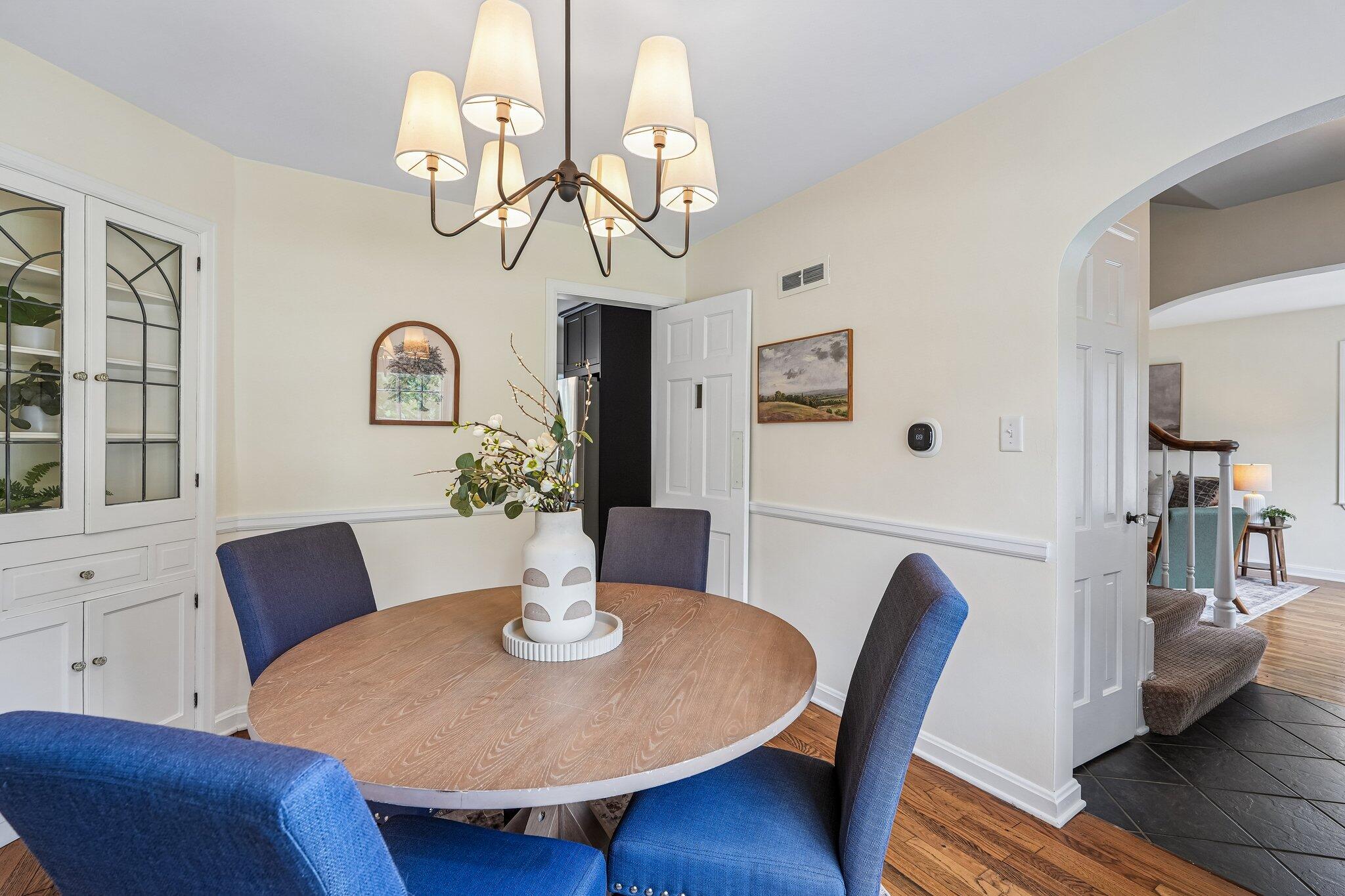 Dining room with a round wood table, blue chairs, built-in china cabinet, and chandelier.