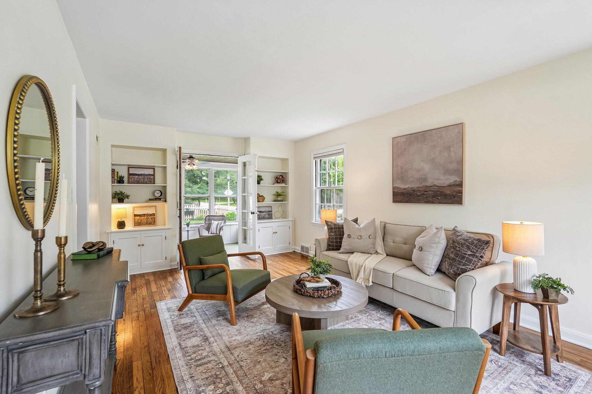 Living room with built-in shelves, hardwood floors, and French doors opening to a garden.
