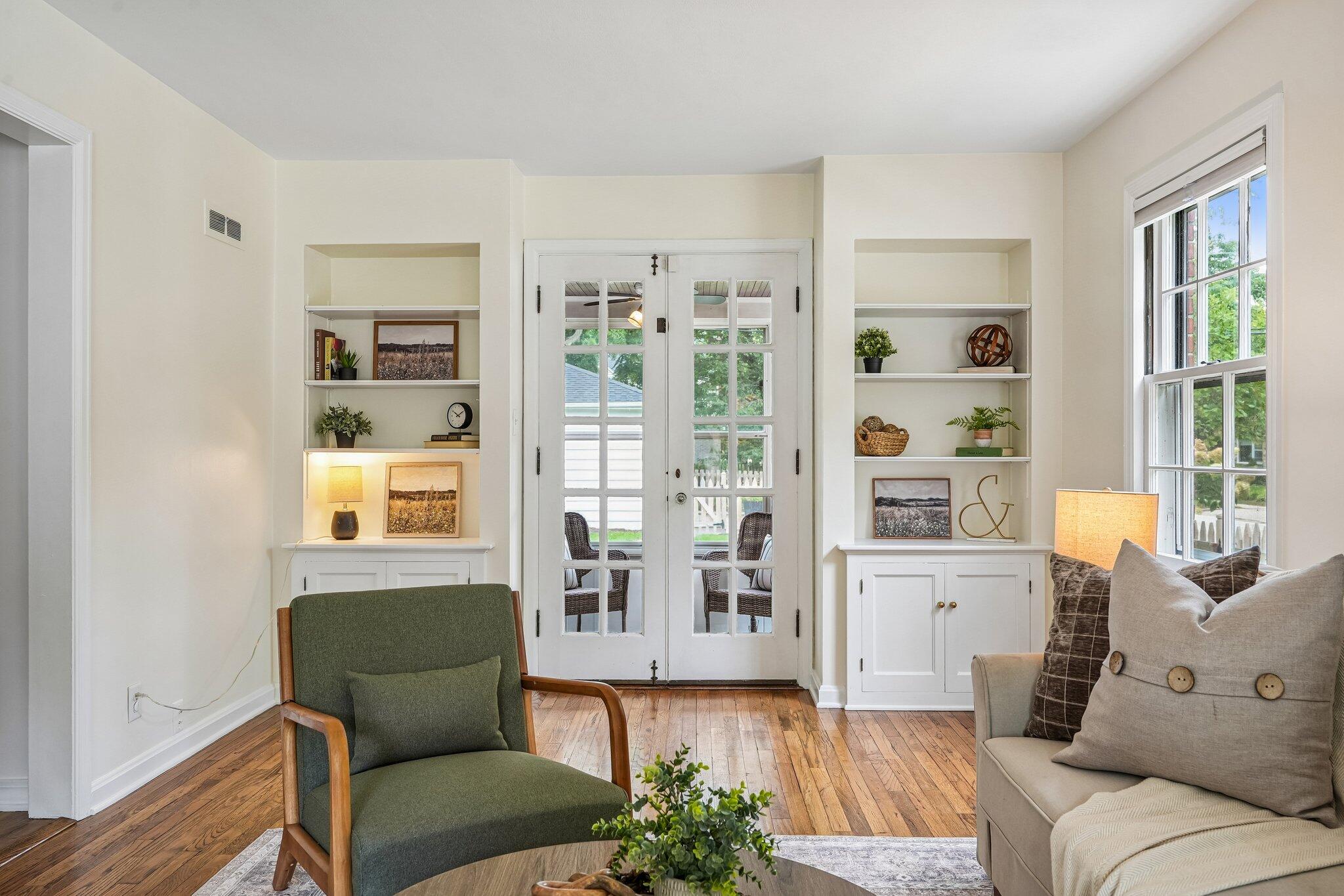 Staged living room with built-in shelves, glass-paneled French doors, and hardwood floors.