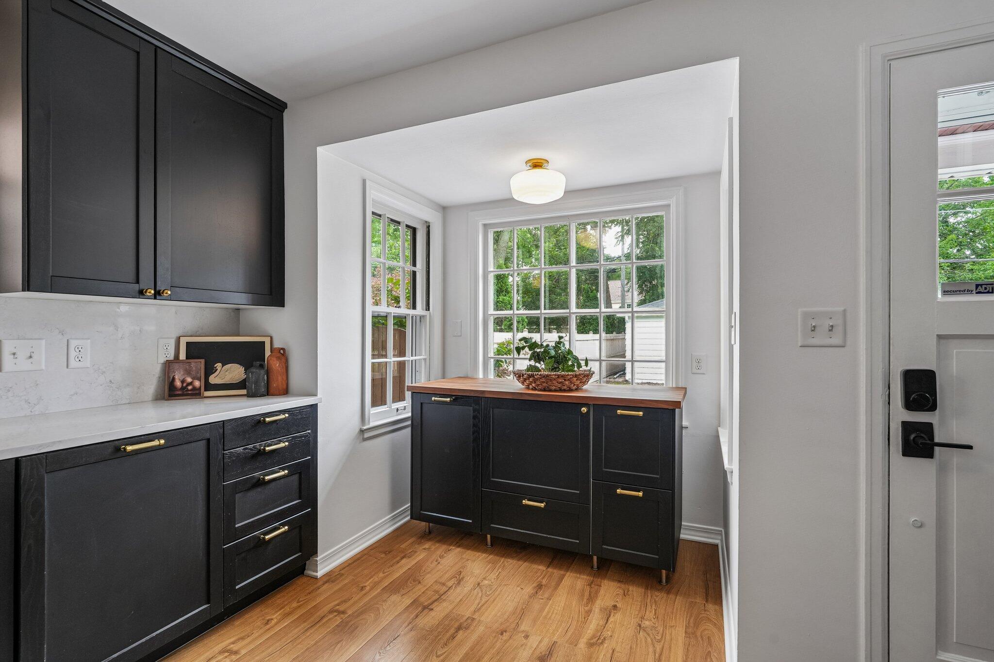 Kitchen with charcoal cabinets, brass hardware, and a butcher-block island beside large windows.