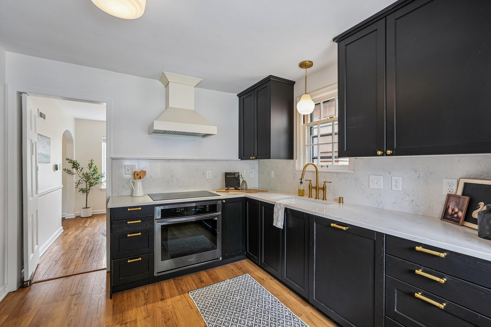 Kitchen with black cabinets, brass hardware, white counters, and warm wood floors.