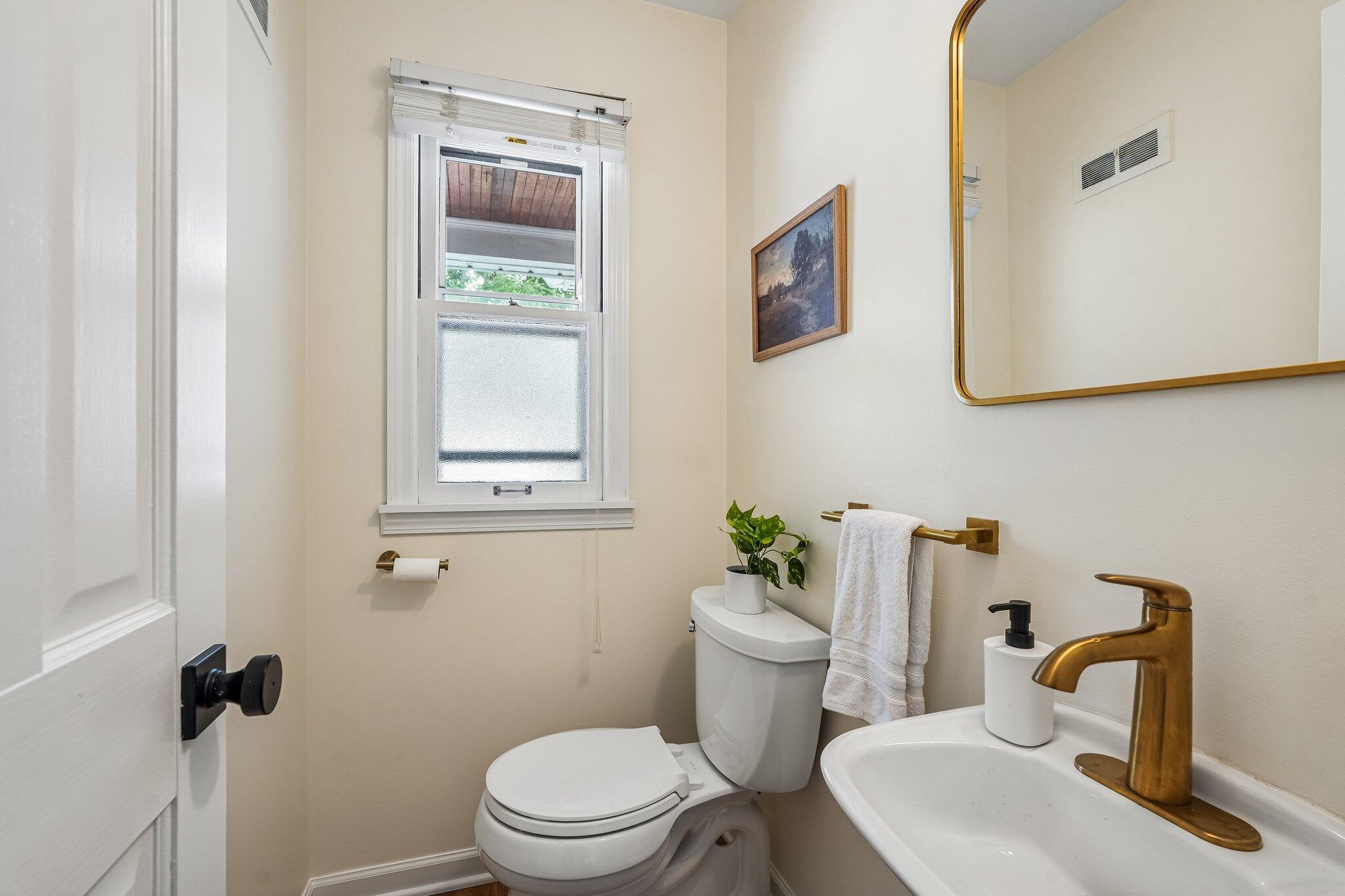 Bathroom with a white toilet and sink, brass fixtures, and a gold-framed mirror.