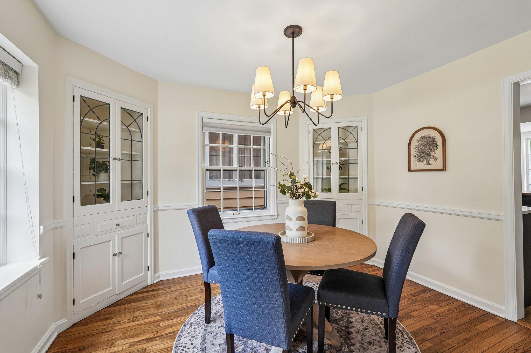 Dining room with a round wooden table, blue chairs, and built-in glass-front cabinets.