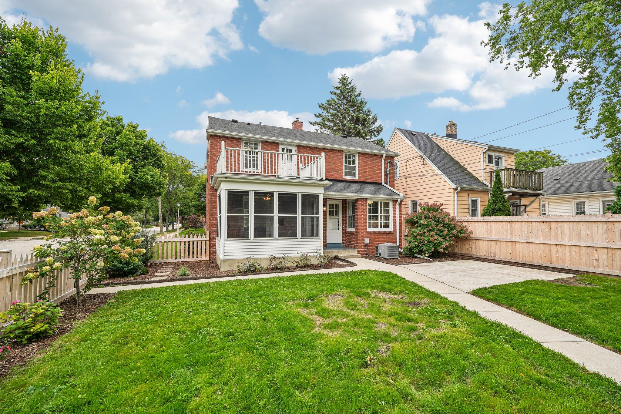 Brick house rear with enclosed porch, upper balcony, backyard lawn, and concrete patio.