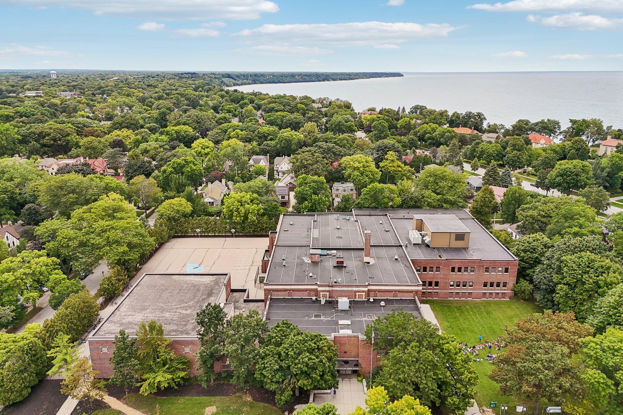 Aerial view of a red-brick building, outdoor court, leafy neighborhood, and shoreline.